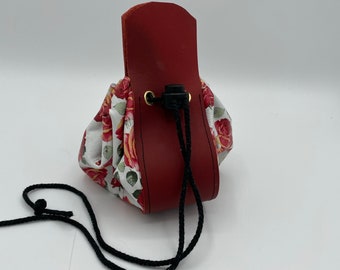 Op de afbeelding: Een klein rood leren trekkoordtasje met een witte bloemenprint. De tas heeft een zwart trekkoord en een leren klep met een metalen gesp.