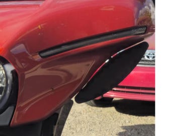 Puede incluir: Un carenado de motocicleta rojo brillante con un diseño aerodinámico y elegante, que presenta una prominente franja de acento horizontal negra y un panel inferior negro curvado. El componente es liso, reflectante y contorneado.