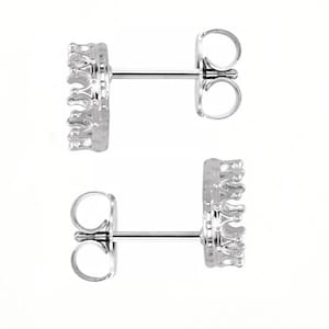 May include: Two silver-colored stud earrings with a crown design. The earrings have a post and butterfly backing. The crown design is detailed with small, raised elements. The background is plain white.