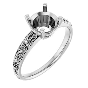 May include: A silver-toned metal ring setting featuring a four-prong head designed to hold a single gemstone. The band displays an intricate, repeating scrollwork pattern along the outer surface, extending from the base of the prongs.