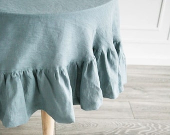 May include: A light blue linen tablecloth with a ruffled edge. The tablecloth is draped over a wooden table.