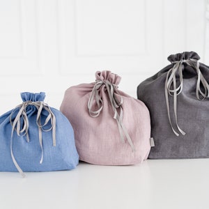 May include: Three linen drawstring bags in different colors: blue, pink, and gray. The bags are made of a soft, natural fabric and have a simple, elegant design.