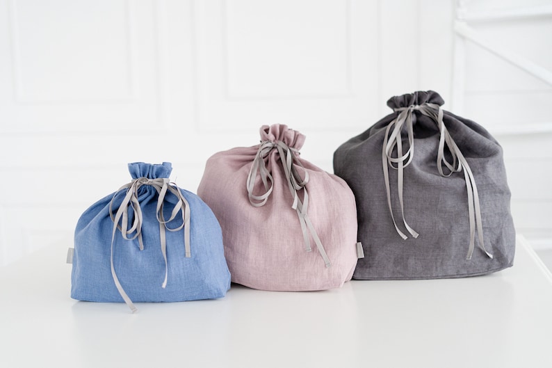 May include: Three linen drawstring bags in different colors: blue, pink, and gray. The bags are made of a soft, natural fabric and have a simple, elegant design.