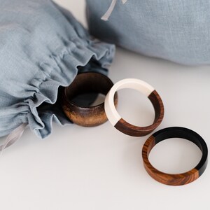 May include: Three wooden bracelets with contrasting colored halves. One bracelet is brown and white, one is brown and black, and one is all brown. The bracelets are on a white surface.