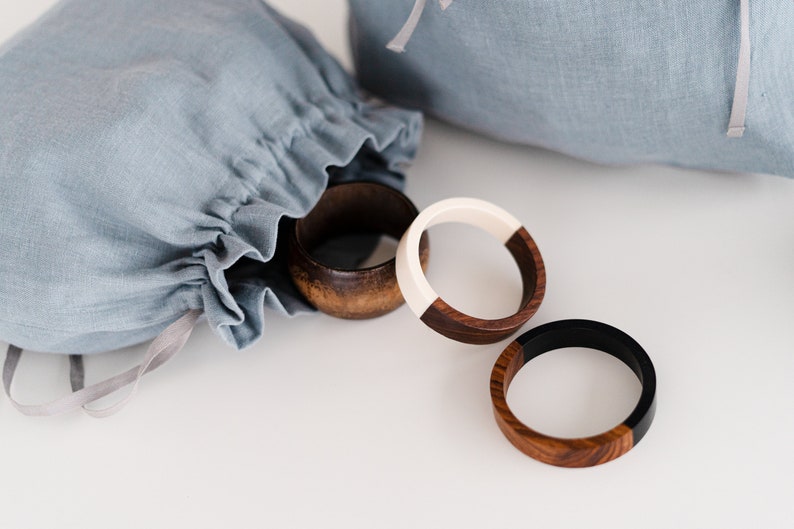 May include: Three wooden bracelets with contrasting colored halves. One bracelet is brown and white, one is brown and black, and one is all brown. The bracelets are on a white surface.