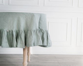 May include: A sage green linen tablecloth with a ruffled edge, draped over a round table with wooden legs.