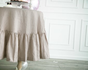 May include: A beige linen tablecloth with a ruffled edge. The tablecloth is draped over a round table and is set for a party.