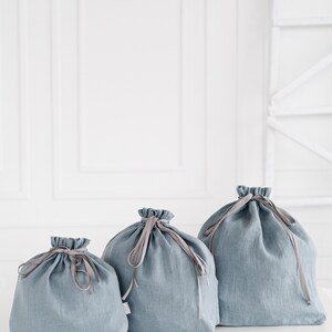 May include: Three blue linen drawstring bags of different sizes. The bags have a light blue color and are made of a soft, natural fabric. The bags are perfect for storing small items or gifts.
