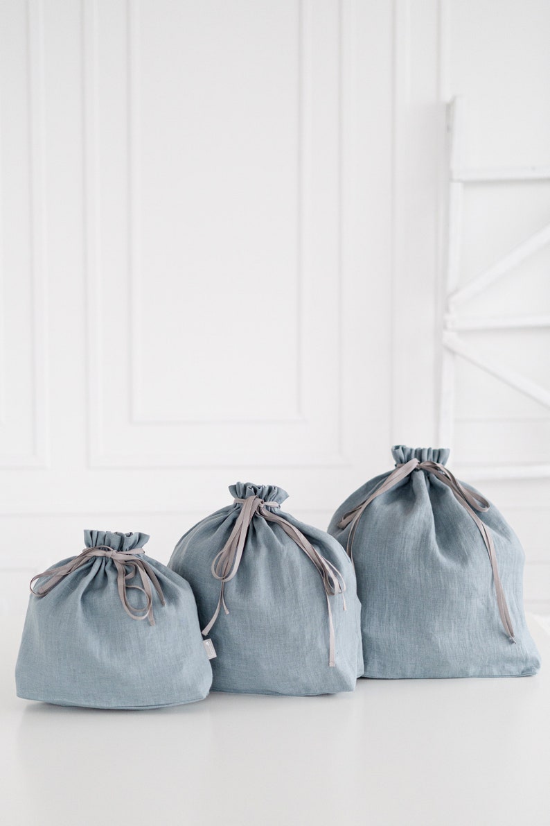 May include: Three blue linen drawstring bags of different sizes. The bags have a light blue color and are made of a soft, natural fabric. The bags are perfect for storing small items or gifts.