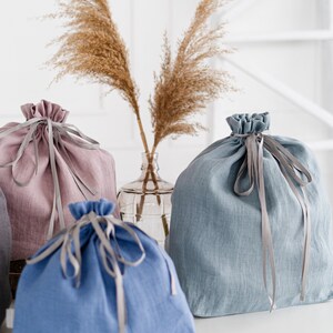 May include: Three fabric drawstring bags in different colors. A light pink bag, a light blue bag, and a darker blue bag. Each bag has a gray ribbon tied around it.