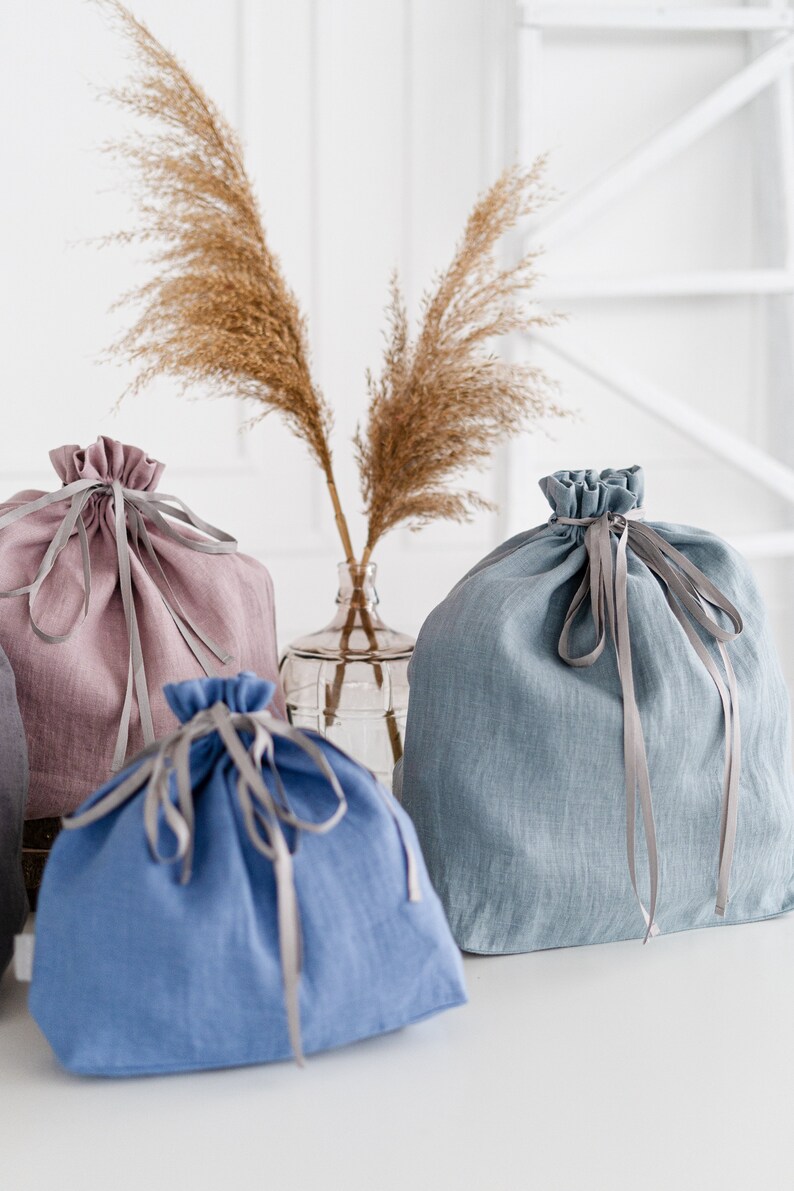 May include: Three fabric drawstring bags in different colors. A light pink bag, a light blue bag, and a darker blue bag. Each bag has a gray ribbon tied around it.