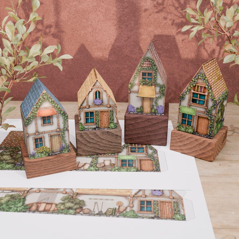 Front view of 4 finished models of paper huts. The huts stand on wooden stands, against the background of a burgundy wall. In the foreground, on a wooden top, there are two sheets of paper, on which printed, not yet folded models can be seen.