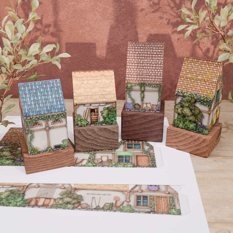 A view of 4 folded paper models of rural huts rotated so that they can be seen from the right side. The huts stand on wooden stands of different heights. On the bright countertop, there are two printed sheets with not yet folded models of houses. The houses contain many details such as vegetation, bushes, and flowers. Their walls are abundantly braided with ivy. From the right side, you can also see such details as wooden lockers against the wall, bags, barrels, and gardening tools.