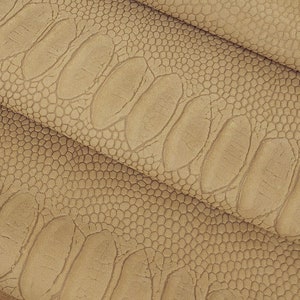 May include: Close-up of a folded piece of brown faux leather with an embossed crocodile pattern.