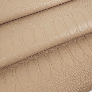 Könnte beinhalten: Beigefarbener Kunstlederstoff mit einem geprägten Krokodilmuster. Der Stoff ist dreifach gefaltet und zeigt das Muster aus verschiedenen Blickwinkeln.