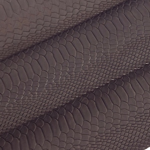 Peut inclure: Gros plan sur un tissu en cuir gaufré effet peau de serpent brun. Le tissu est plié en trois, montrant la texture et le motif.