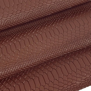 Könnte beinhalten: Braunes Kunstledergewebe mit Schlangenhautmuster. Der Stoff ist aufgerollt und dreifach gefaltet.