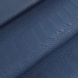 May include: Close-up of a stack of blue leather fabric with a textured, embossed pattern. The fabric has a subtle sheen and a slightly raised, scaly texture.