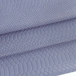May include: A close-up of a piece of light purple faux snakeskin fabric. The fabric has a textured surface that resembles snake scales.