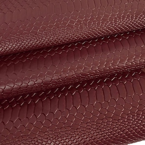 Peut inclure: Gros plan sur un tissu en cuir imitation peau de serpent de couleur bordeaux. Le tissu a une surface texturée qui ressemble à des écailles de serpent.