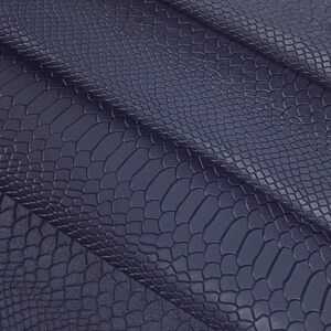 Op de afbeelding: Close-up van een donkerblauwe, textuurrijke stof met een slangenhuidpatroon.