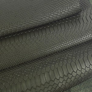 Könnte beinhalten: Nahaufnahme von schwarzem Kunstleder im Schlangenhautmuster. Der Stoff ist in mehreren Lagen gefaltet, wodurch die Textur und das Muster sichtbar werden.