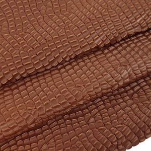 Puede incluir: Primer plano de una tela marrón texturizada con un patrón escamoso. La tela está doblada en tres partes, revelando la textura y el patrón.