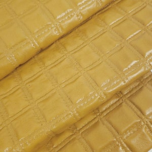 May include: A close-up of a stack of mustard yellow quilted fabric. The fabric has a square quilted pattern.