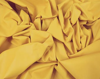 May include: A close-up of a crumpled piece of yellow leather fabric. The fabric is a solid, vibrant yellow color, with visible folds and creases. The edges of the leather are slightly rough, showing the natural texture of the material.