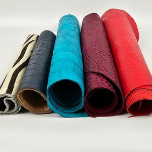 Puede incluir: Seis rollos de cuero de diferentes colores y estampados. Los cueros están enrollados y dispuestos en una fila. Los cueros están en el siguiente orden de izquierda a derecha: estampado de cebra, estampado de cocodrilo azul oscuro, azul turquesa, estampado de leopardo y rojo.