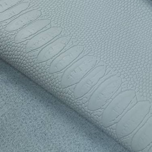 May include: Close-up of a light blue faux leather fabric with a textured alligator skin pattern.