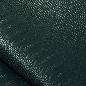 May include: Close-up of dark green faux leather fabric with an embossed crocodile pattern. The fabric is folded over itself, showing the texture and detail of the pattern.