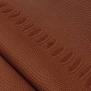 Puede incluir: Primer plano de una tela de cuero marrón con un patrón texturizado de piel de cocodrilo.