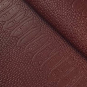 Könnte beinhalten: Nahaufnahme eines burgunderfarbenen Kunstleders mit einem geprägten Krokodilmuster.