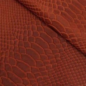 Puede incluir: Primer plano de una tela texturizada con un patrón de piel de serpiente en un color marrón rojizo profundo.