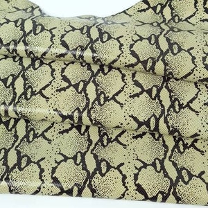 Può includere: Un tessuto beige con un motivo a pelle di serpente nero. Il tessuto è piegato e testurizzato.