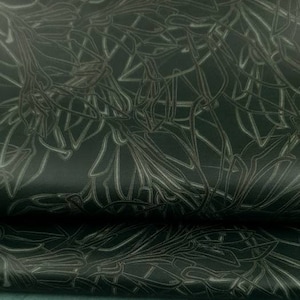 Op de afbeelding: Donkergroen leer met een bloemmotief in reliëf op de bovenste laag. De onderste laag is effen teal groen. Het leer is omgevouwen en onthult de twee verschillende texturen en kleuren.