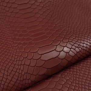 May include: Close-up of a burgundy faux leather fabric with a crocodile embossed pattern.