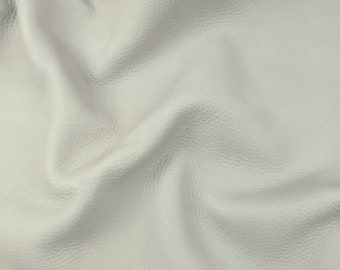 May include: A close-up of a piece of off-white leather with a textured surface. The leather is folded and draped, showing its soft and supple texture.