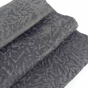 May include: Close-up of several sheets of dark gray, textured fabric. The fabric has a crinkled, leaf-like pattern, creating a unique, three-dimensional effect. The material appears to be soft and pliable, suitable for various craft projects.