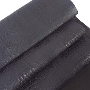 May include: Close-up of dark gray alligator embossed leather. The leather is folded in thirds, showing the texture and grain.