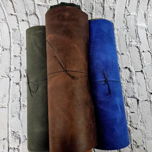 May include: Three rolls of leather in different colours: dark green, brown, and blue. The leather is rolled up and tied with string.