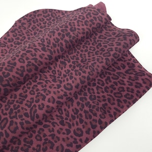 Könnte beinhalten: Ein gefaltetes Stück Stoff mit einem dunkelburgunderfarbenen und schwarzen Leopardenmuster. Das Textil zeigt ein sich wiederholendes Tierfleckenmuster auf der Oberfläche, wobei der Stoff in weichen Falten drapiert ist, um Textur und Kontrast zu zeigen.