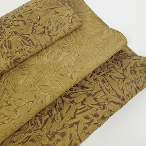 May include: Close-up of folded sheets of textured, tan-colored material. The material has a raised, organic pattern in a darker brown hue, creating a contrast. The sheets are layered, revealing the texture and color variations.