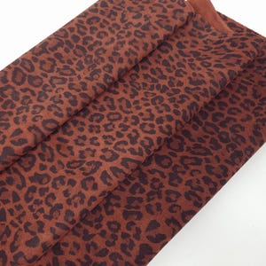 Puede incluir: Tela doblada con estampado de leopardo marrón. La tela tiene una base marrón rojizo con manchas marrón oscuro. El material parece suave y texturizado. Estampado animal clásico.