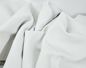 May include: Close-up of white leather fabric with a textured surface. The leather is draped and folded, creating shadows and highlights. The material appears soft and supple, suitable for various crafting projects.