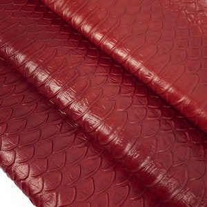 May include: Red leather with a textured, scaly pattern. The leather is folded in a few places, showing the texture from different angles.