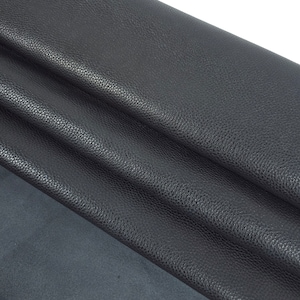Puede incluir: Primer plano de tela de cuero texturizada negra doblada en tres. La tela tiene una superficie granulada y una sensación suave y flexible.