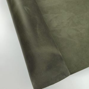 Peut inclure: Un rouleau de cuir vert olive. Le cuir présente une surface texturée avec des variations de couleur, créant un aspect vieilli. Le matériau est partiellement enroulé, révélant le dessous et les bords.