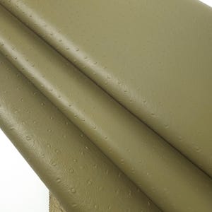 May include: Close-up of a folded piece of light brown leather with a textured, ostrich-like pattern.